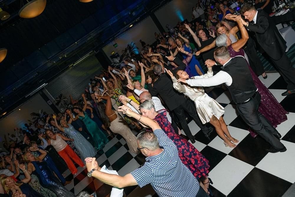 Guests dancing with arms raised on a checkerboard dancefloor