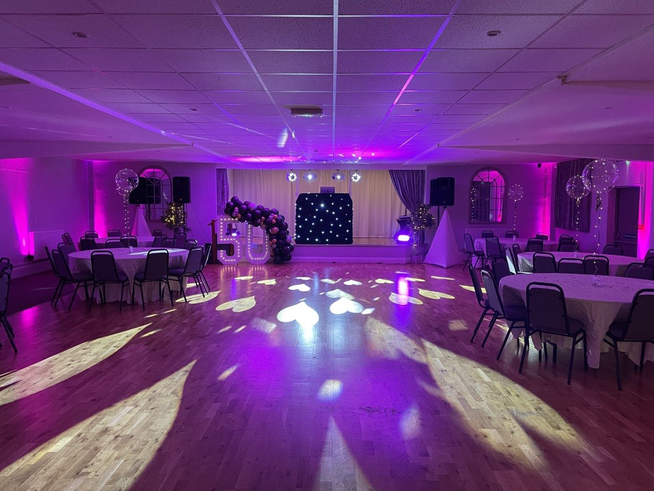 Function room dressed for a 50th birthday party with pink uplighting