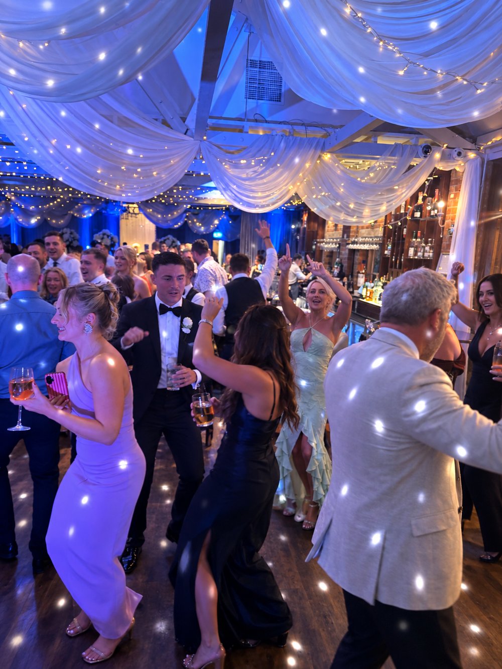 Guests dancing together beneath draped lights at a celebration
