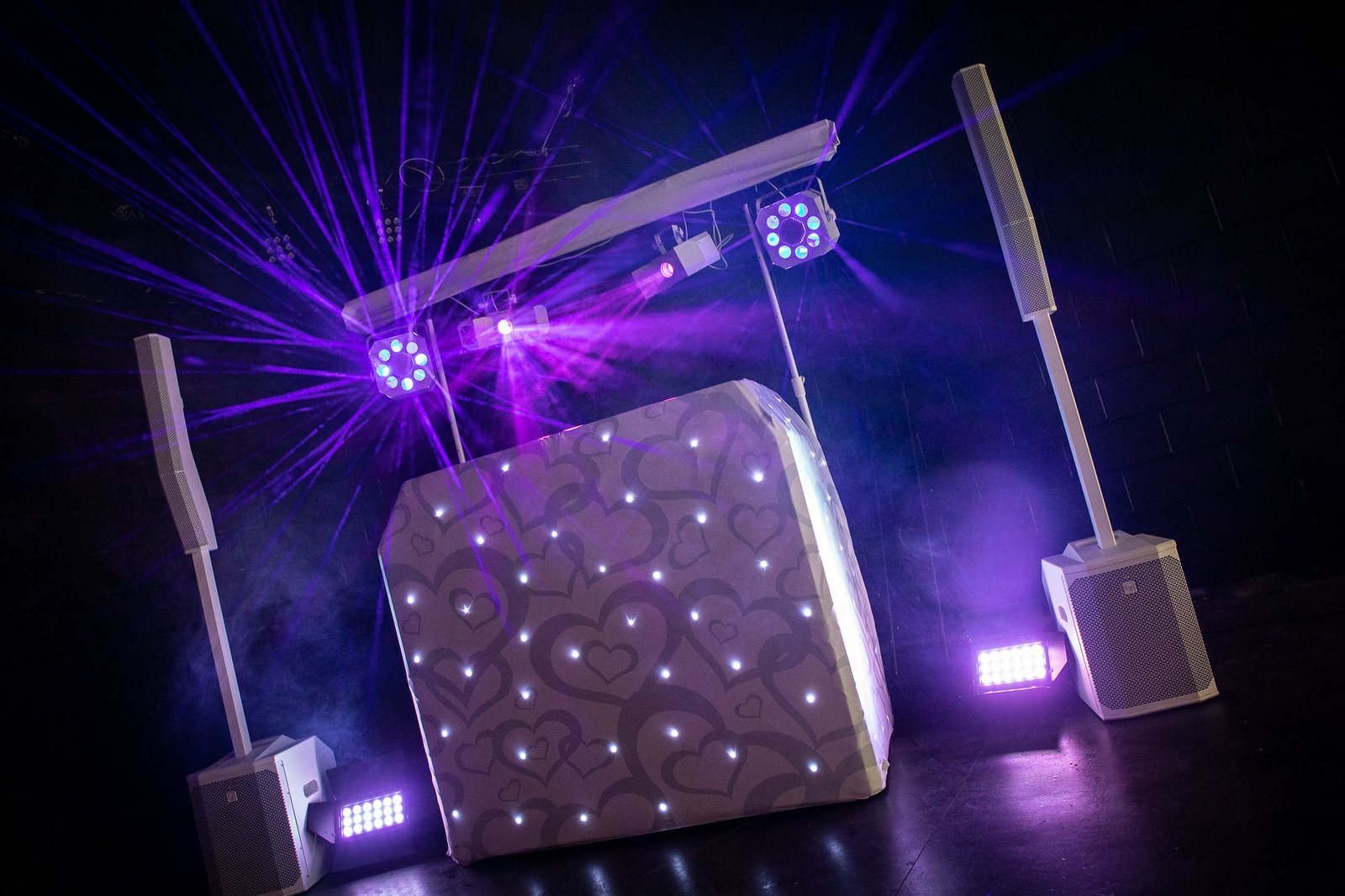 White DJ booth and sound system under purple laser lighting