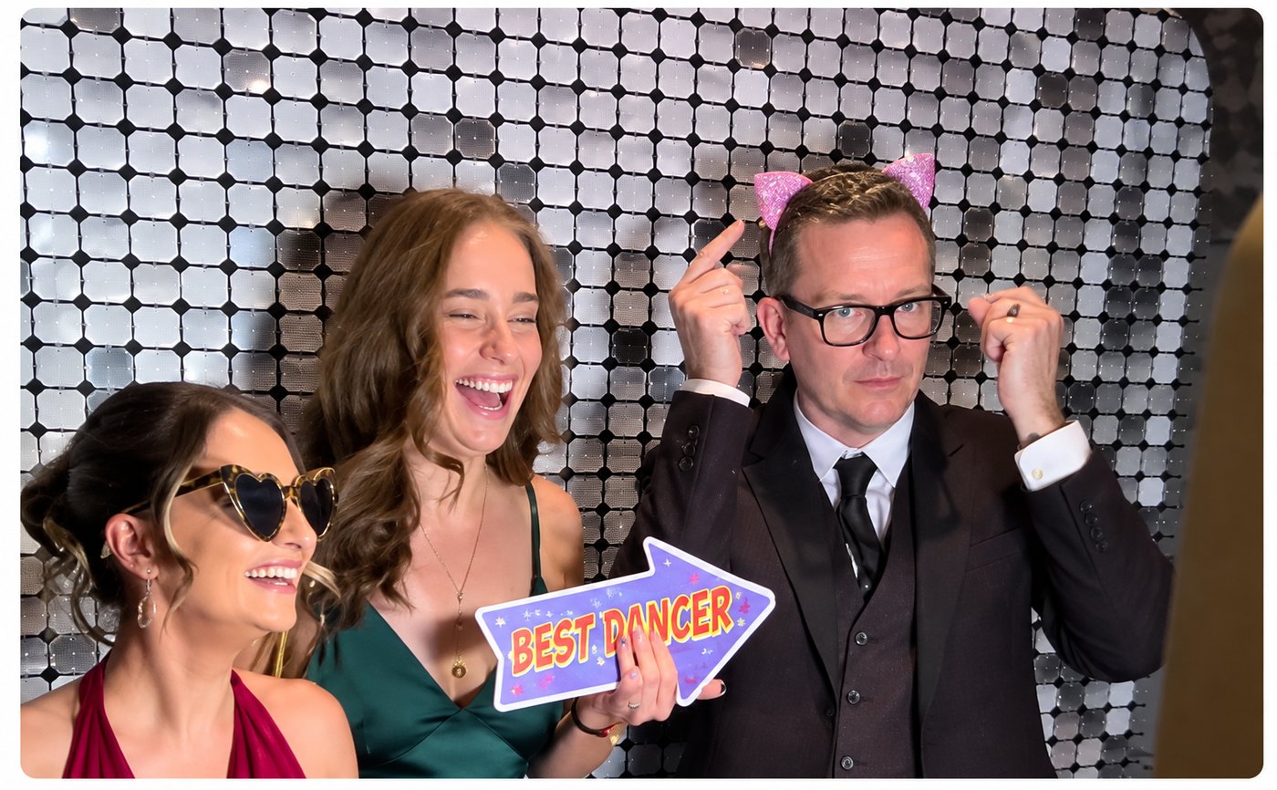 Three guests choosing props in front of a silver photo backdrop
