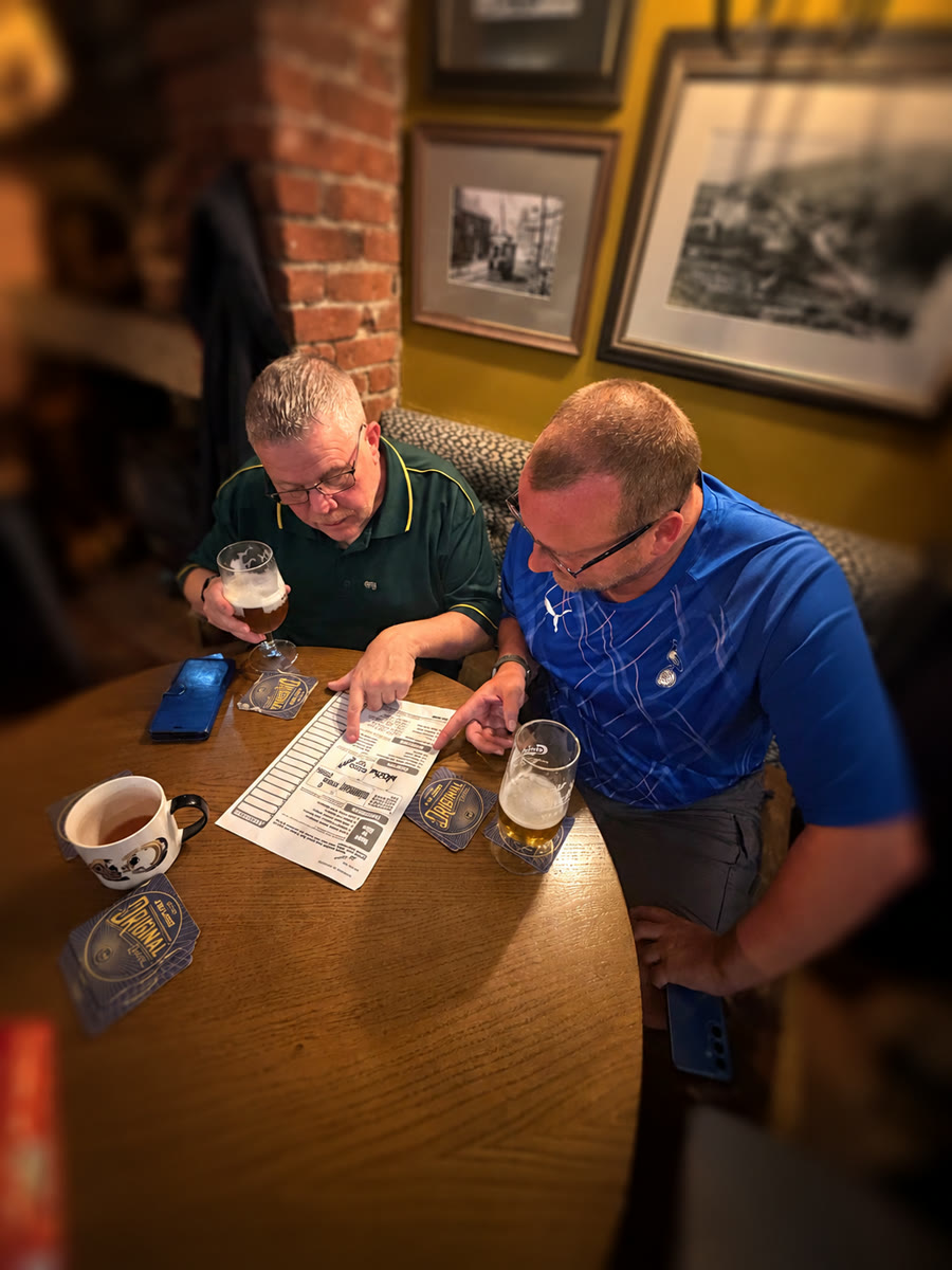 Two men completing a quiz sheet at a hosted quiz night