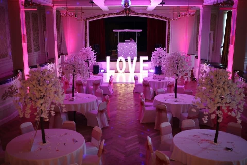 Wedding reception room dressed with floral centrepieces and a light-up LOVE sign