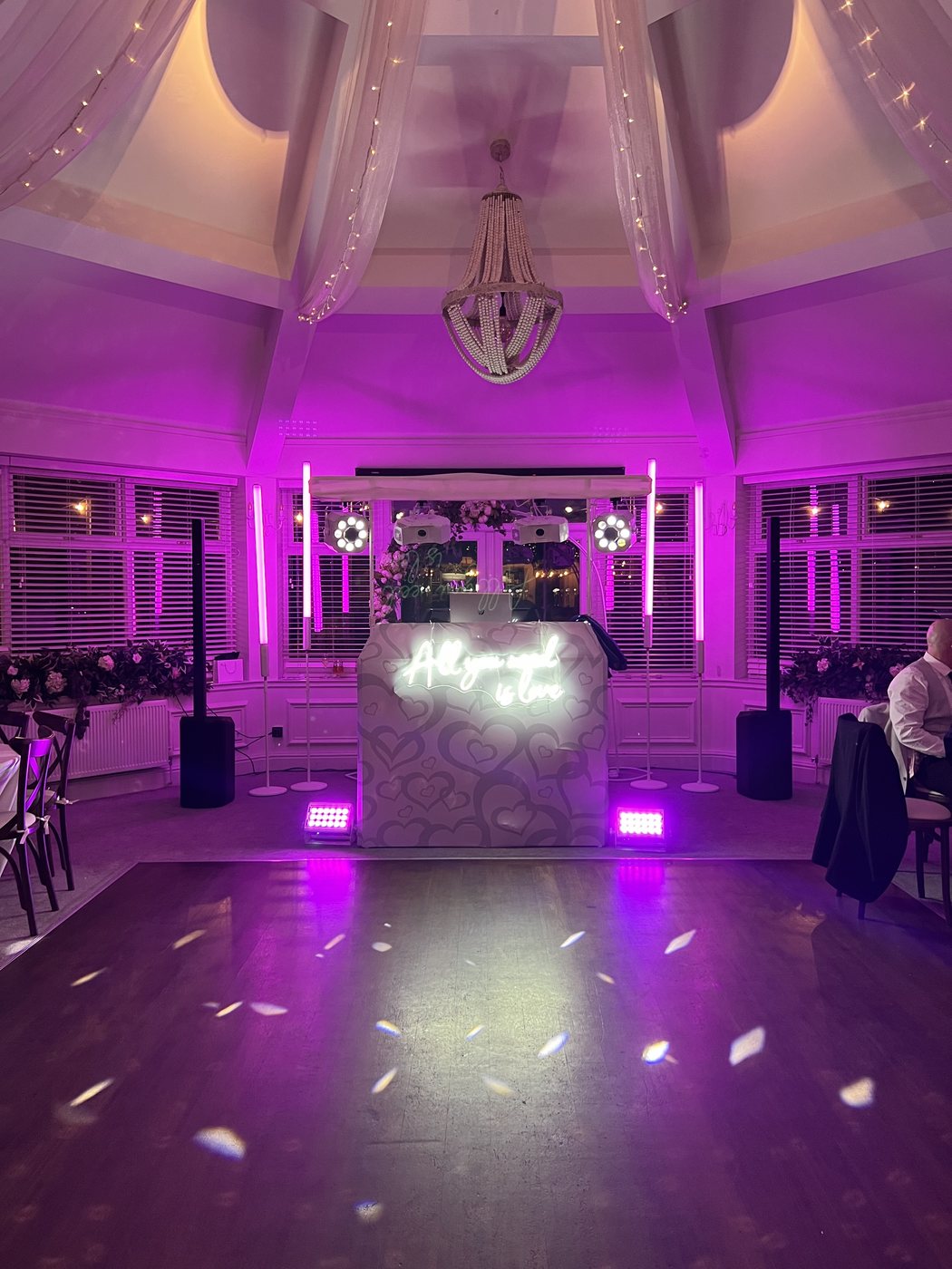 Wedding DJ setup with pink uplighting in a bright reception room